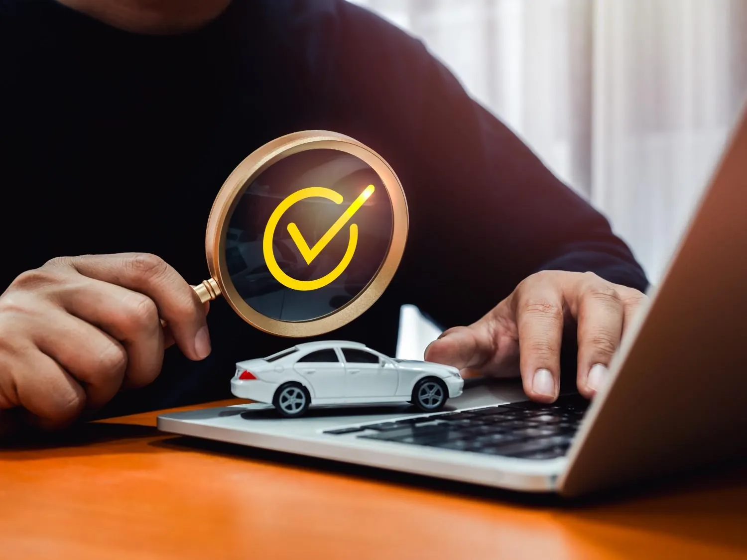 Magnifying glass with a check mark over a toy car on a laptop